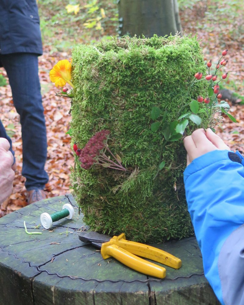Eine Kinderhand steckt Beeren in eine Urne aus Moos