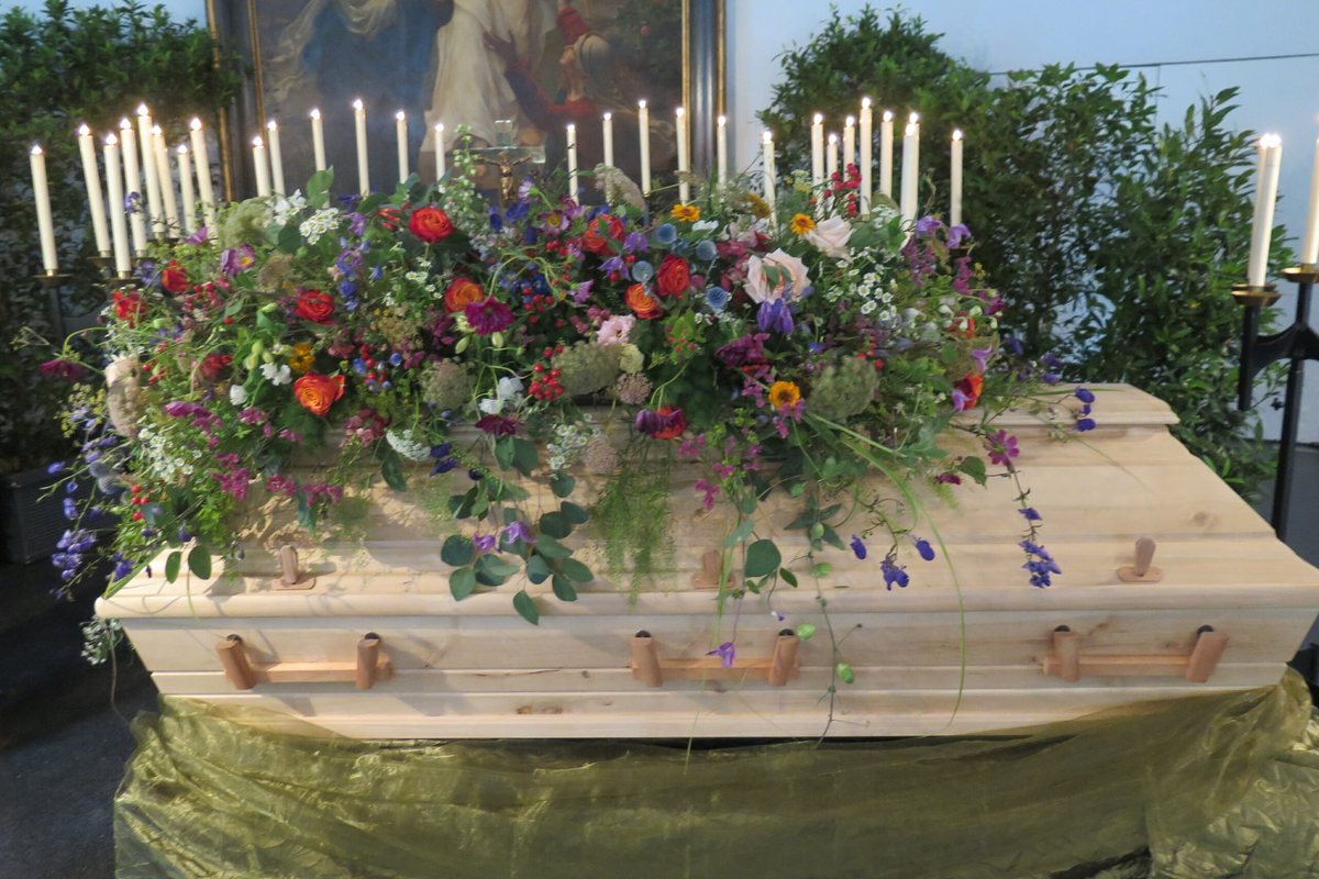 Heller Holzsarg mit einem großen Gesteck aus Wiesenblumen