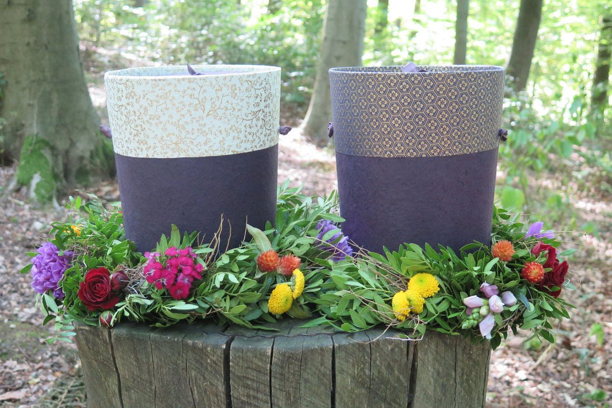 Zwei Papierurnen mit einem bunten Blumenkranz auf einem Baumstumpf im Wald