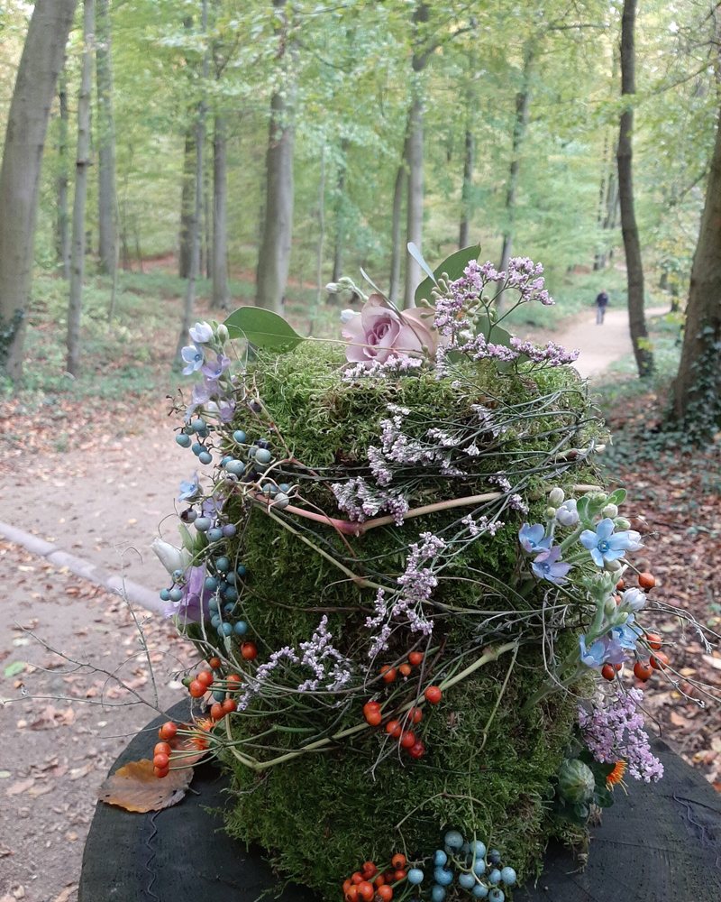 Eine mit Blumen geschmückte Urne aus Moos auf einem Baumstumpf im Wald